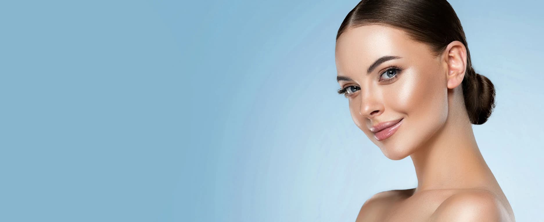 A bare shouldered woman with hair tied back in a bun head turned smiling out of the screen.